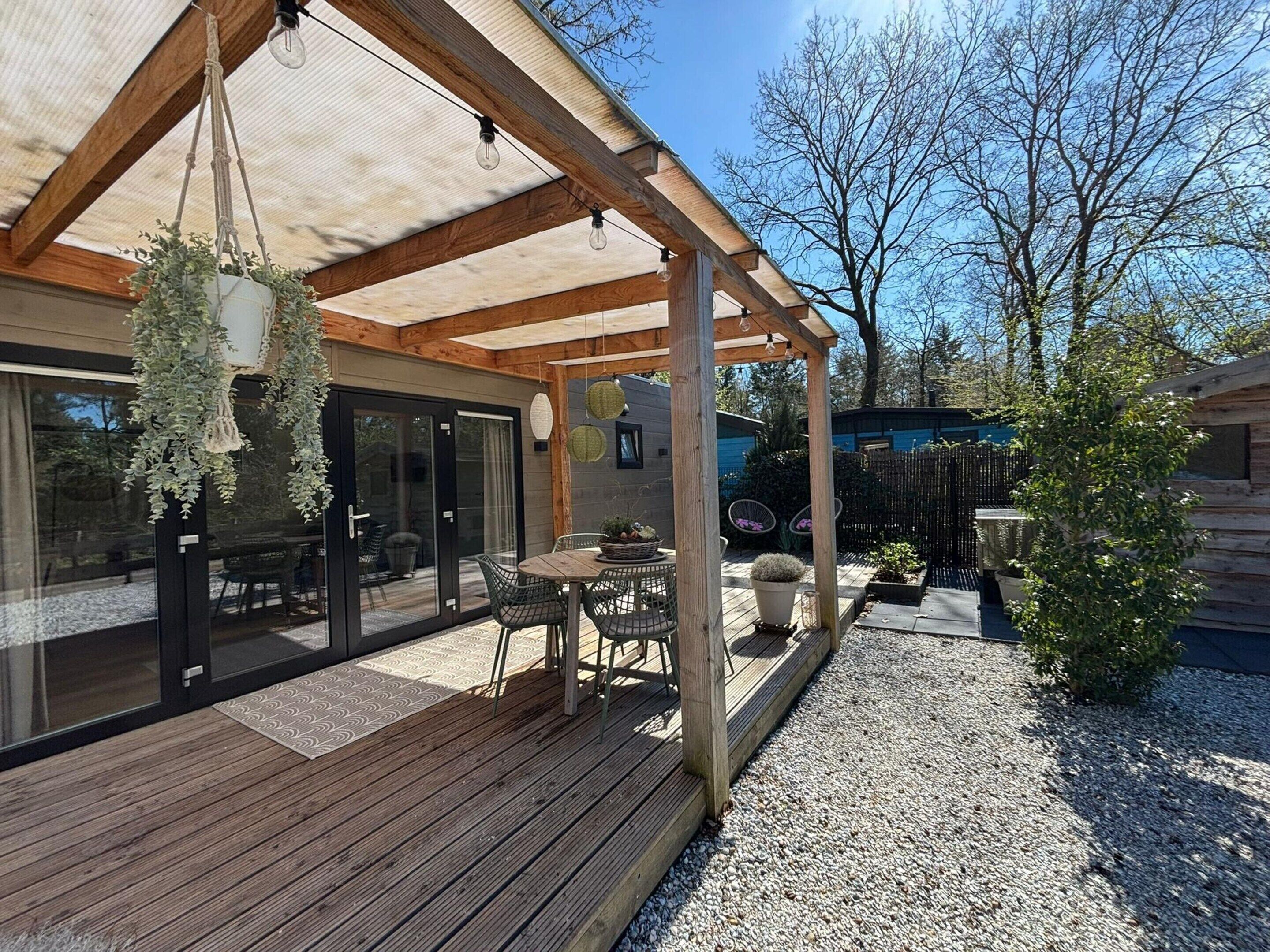 En overdækket terrasse med træterrasse, udendørs møbler og hængende planter.