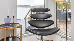 Une pièce moderne avec un fauteuil noir à plusieurs niveaux, une petite table ronde ornée d’une bougie et d’une bouteille, et un lampadaire.