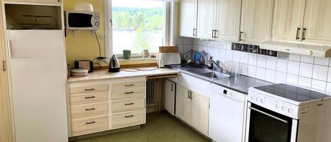 Una cocina con armarios blancos, microondas, estufa y ventana con vistas a la vegetación.
