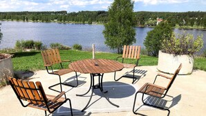 A patio with a round table and four wooden chairs, overlooking a lake with houses in the background. - 4 Person Holiday Home in Burtrask (Burträsk)
