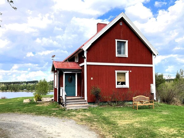 Ein rotes Haus mit grüner Tür, einer kleinen Veranda und einer Bank davor.