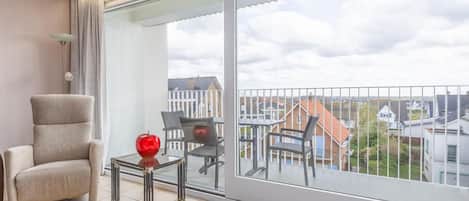 Een modern balkon met uitzicht op woongebouwen, een gewatteelde stoel, een klein tafeltje en een decoratieve appel.