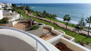 A balcony with a view of the ocean, a patio area with seating, and a pathway leading to the beach. - Beach Penthouse Bermuda Beach 4 (Estepona)