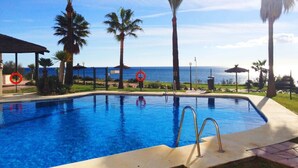 A swimming pool with a view of the ocean, surrounded by palm trees and a clear sky. - Beach Penthouse Bermuda Beach 4 (Estepona)