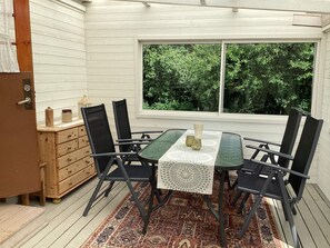 A dining area with a table and chairs, a window with a view of greenery, and a wooden chest of drawers.