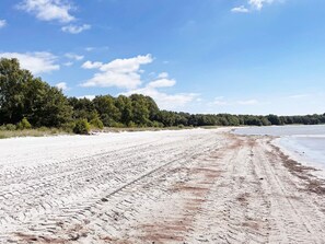 A sandy beach with tire tracks leading to the water, surrounded by dense greenery. - 5 Person Holiday Home in Solvesborg (Sölvesborg)