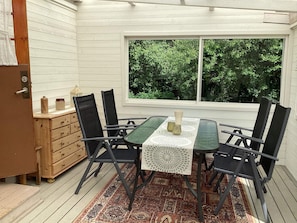 A dining area with a table and chairs, a window with a view of greenery, and a wooden chest of drawers. - 5 Person Holiday Home in Solvesborg (Sölvesborg)