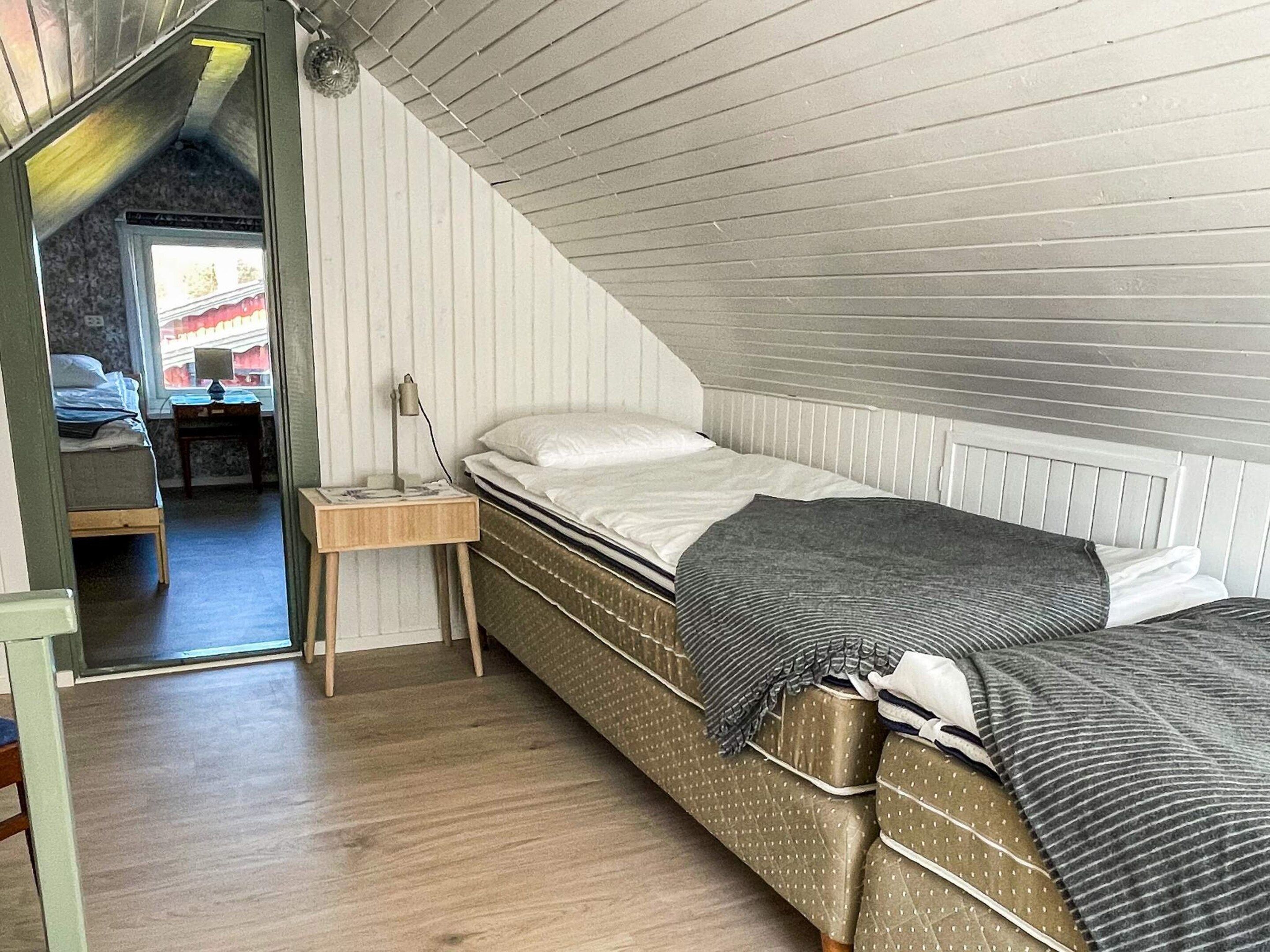 A small, cozy attic bedroom with a sloped ceiling, a single bed, a bedside table, and a window.