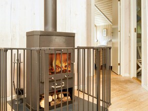 A wood-burning stove with a metal railing in front, logs inside, and a wooden floor. - 6 Person Holiday Home in Graested (Graested)