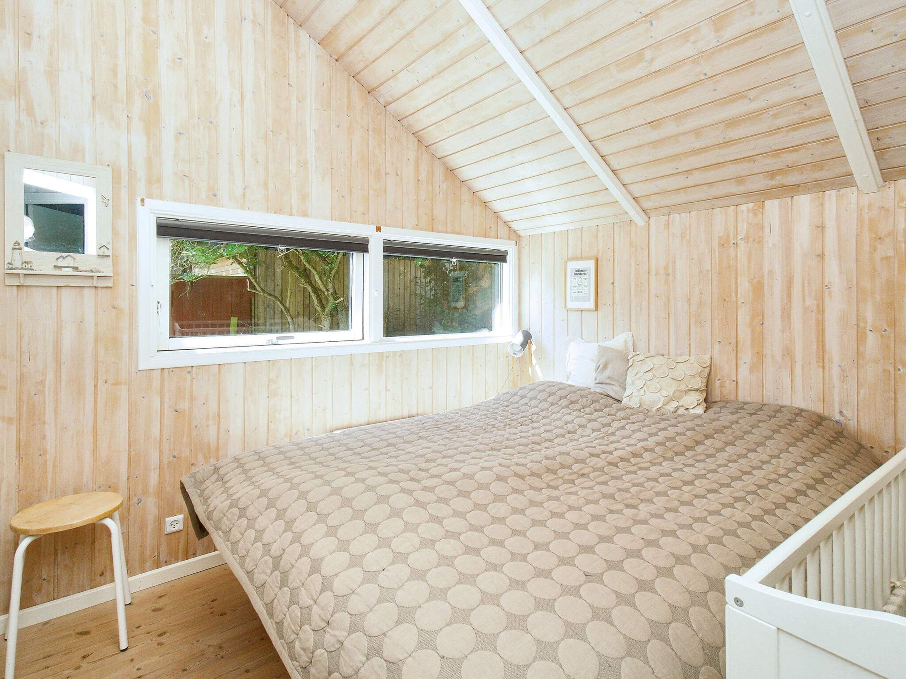 Une pièce aux murs lambrissés, contenant un lit, une fenêtre, un petit tabouret et un berceau.