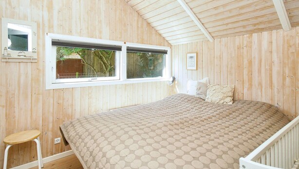 A wooden-paneled room with a bed, a window, a small stool, and a crib. - 6 Person Holiday Home in Graested (Graested)