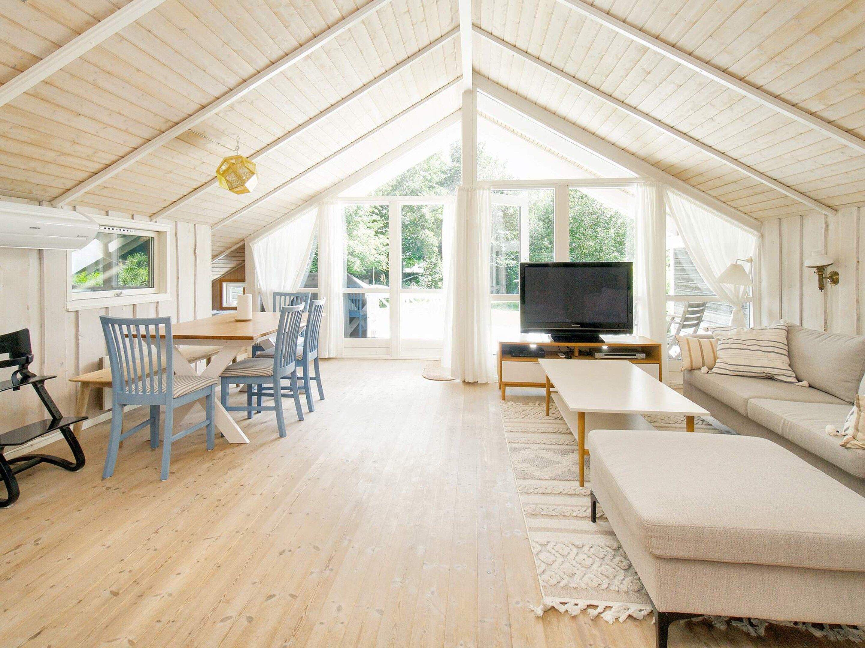 A spacious living area with a high ceiling, a television, a sofa, and a dining table with chairs.