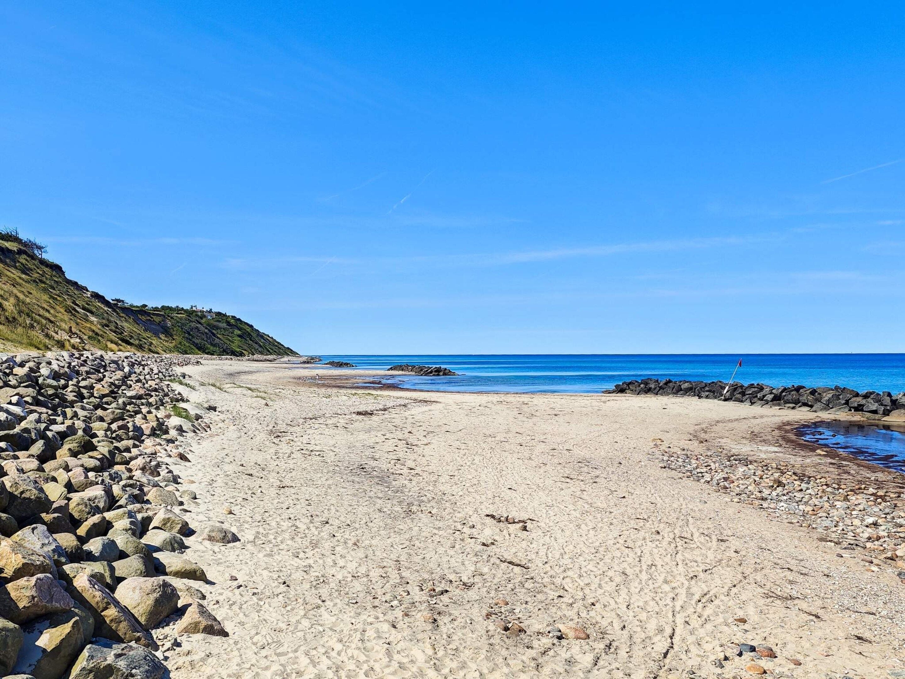 A beach with a rocky shoreline, clear blue sky, and calm sea.