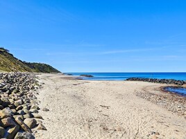 En strand med en klippefyldt kystlinje, klar blå himmel og roligt hav.