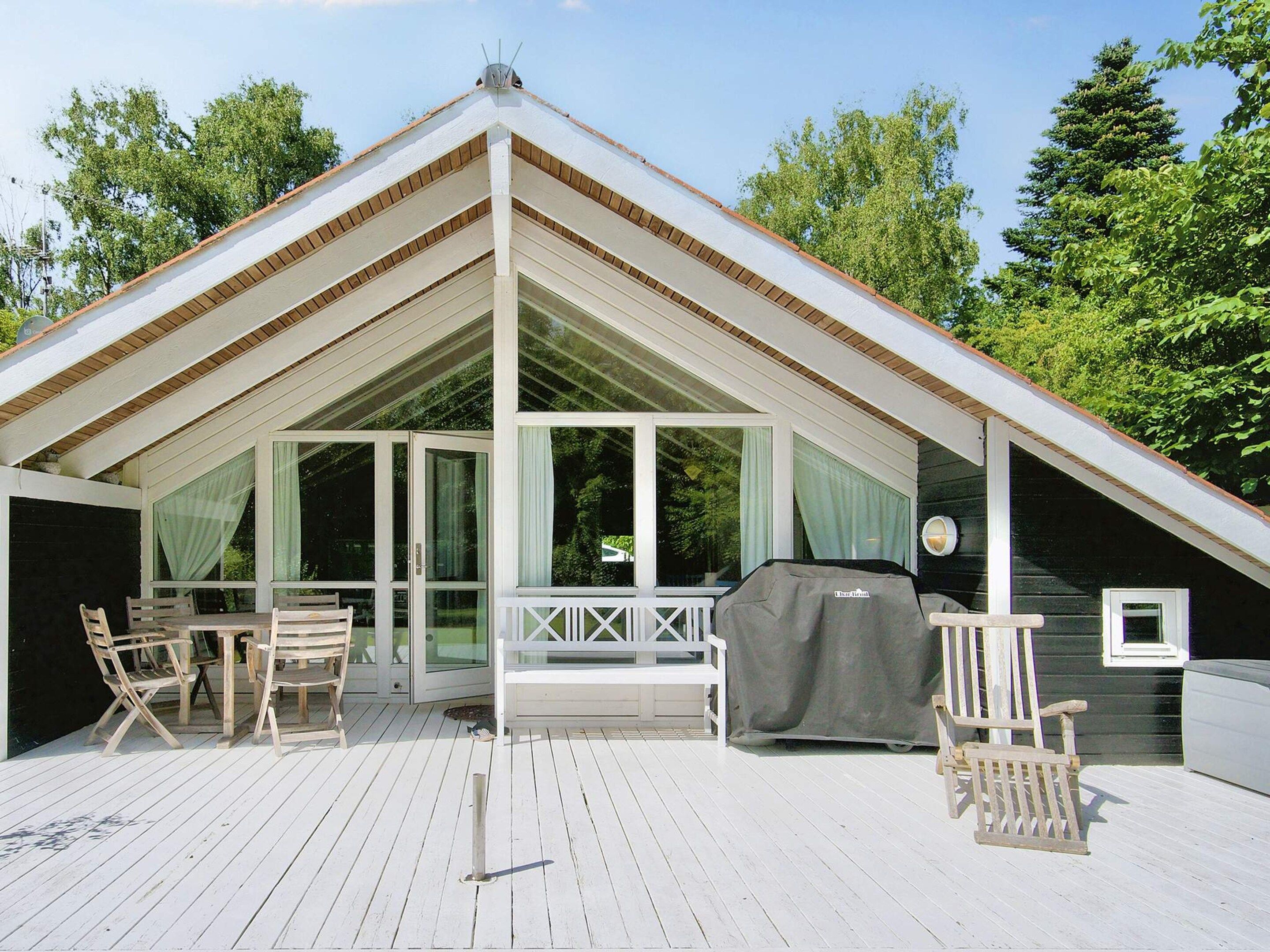 A covered outdoor area with a dining table and chairs, a grill, and a view of the surrounding greenery.