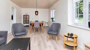 A modern living room with a dining area, grey armchairs, a black coffee table, and a small wooden side table with plants. - 4 Star Holiday Home in Farso (Farso)