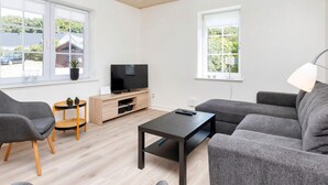 A modern living room with a flat-screen TV, grey sofas, a coffee table, and a small wooden side table with a plant. - 4 Star Holiday Home in Farso (Farso)