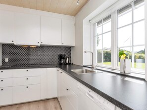 A modern kitchen with white cabinets, a black backsplash, and a large window offering a view of greenery outside. - 4 Star Holiday Home in Farso (Farso)