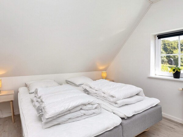A bedroom with a sloped ceiling, a bed with white bedding, two bedside tables with lamps, and a window with a view of greenery. - 4 Star Holiday Home in Farso (Farso)