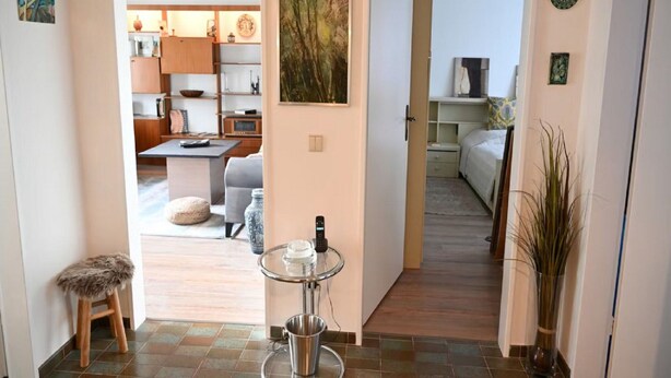 A hallway leading to a living area with a dining table, a sofa, and a small stool. There is a painting on the wall and a vase with plants. - Vintage Style Apartment With Balcony/terrace (Bremen)
