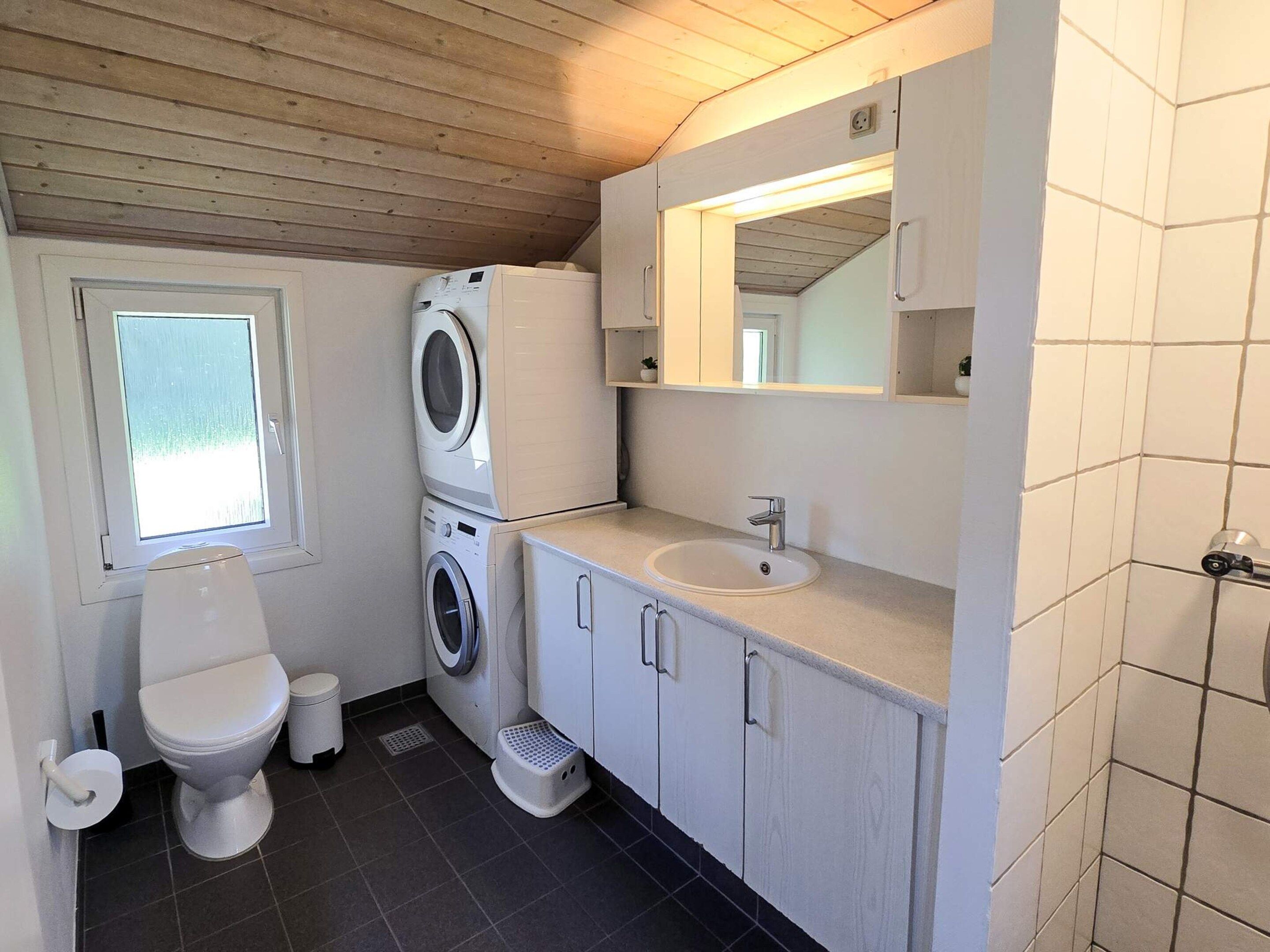 A compact bathroom with a toilet, washing machine, and sink.