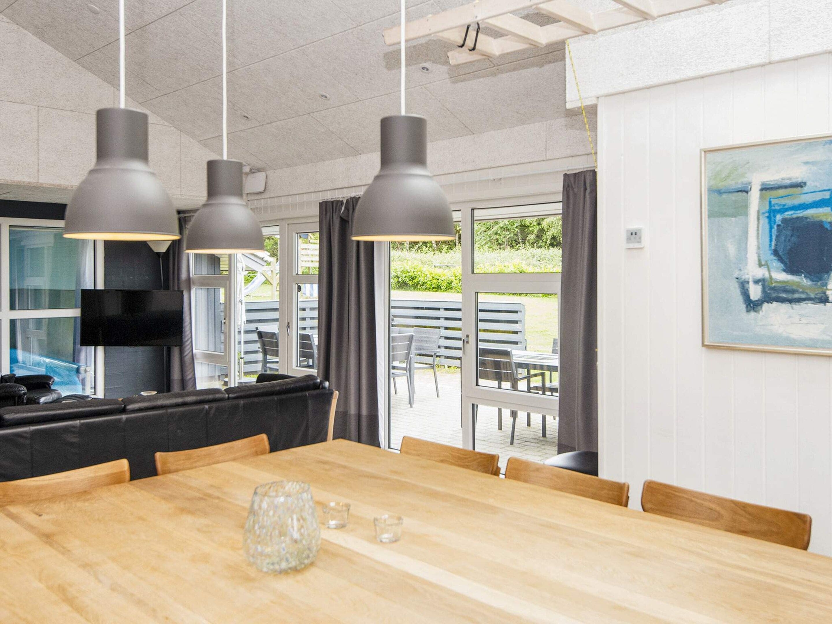 A modern dining area with a wooden table, grey pendant lights, and a television in the background.