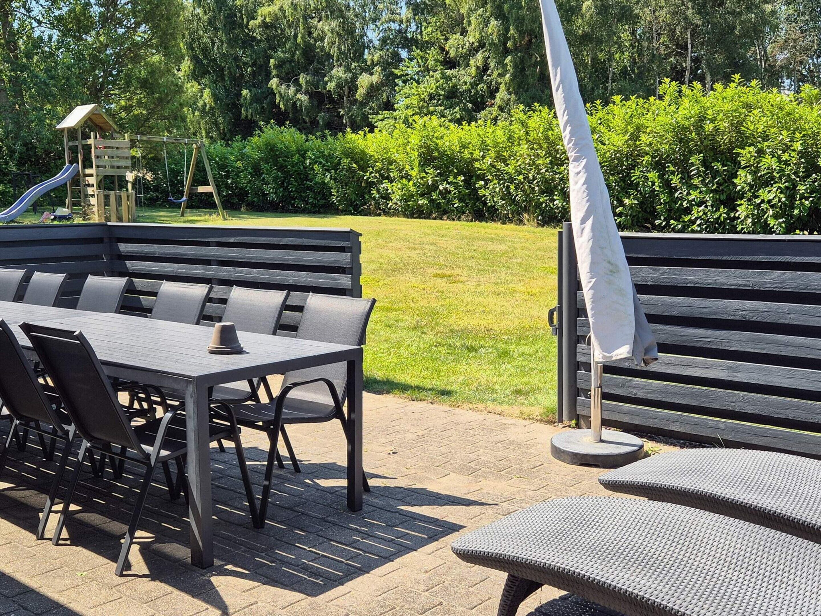 Ein Außenbereich mit Sitzgelegenheit, Tisch, Stühlen, einer Bank und einer Kinderspielanlage.