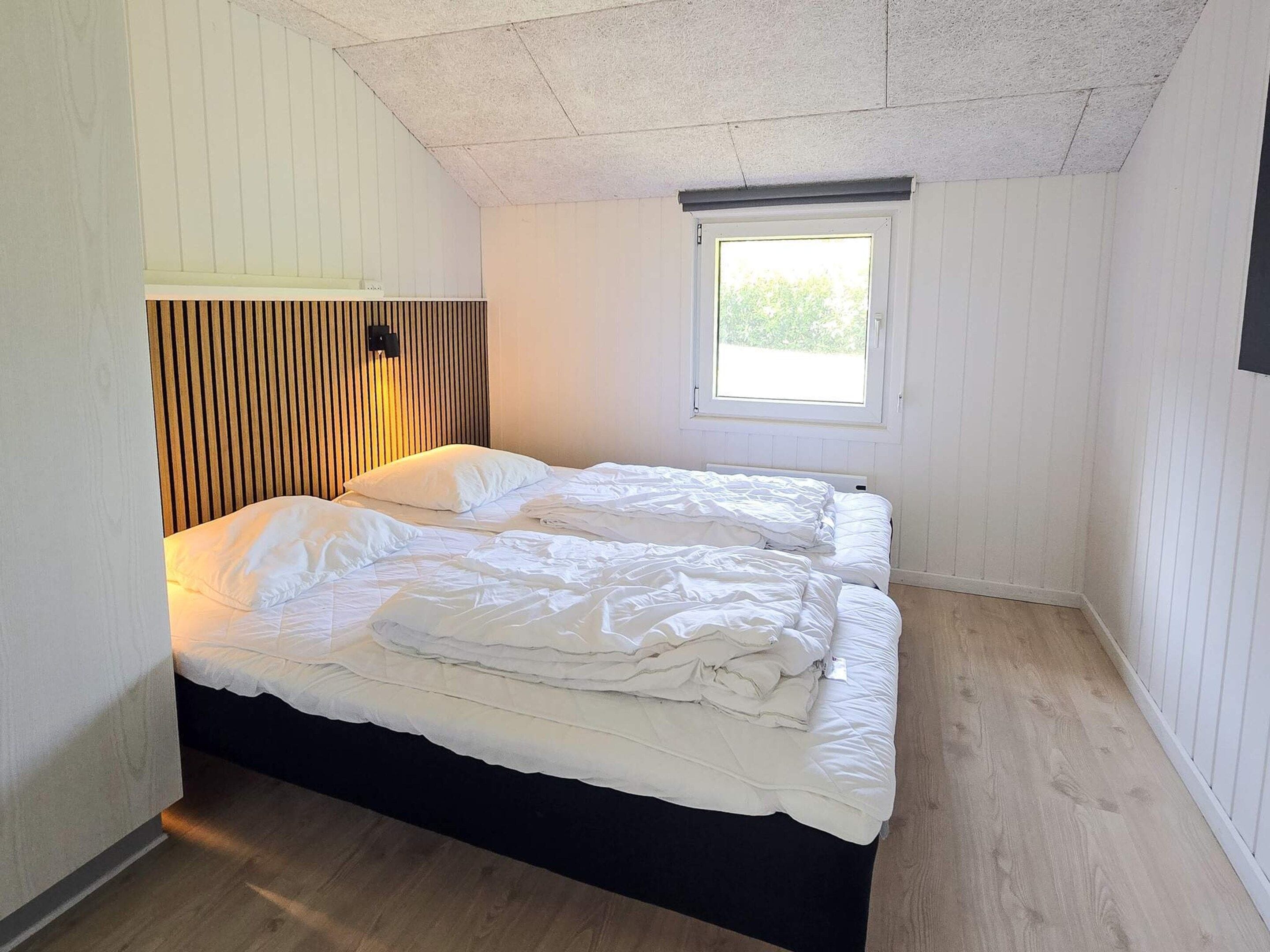 A bedroom with two beds, a window, and wooden paneling on the walls.