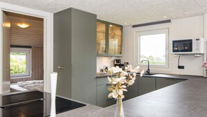 A modern kitchen with a built-in oven, a dining area with a white table, and a view of the outdoors through a window. - 4 Star Holiday Home in Nordborg (Nordborg)