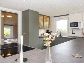 A modern kitchen with a built-in oven, a dining area with a white table, and a view of the outdoors through a window. - 4 Star Holiday Home in Nordborg (Nordborg)