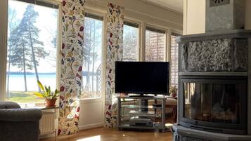 Una sala de estar con chimenea, un televisor sobre un mueble bajo y vistas a un lago a través de amplios ventanales.