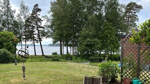 Eine Terrasse mit rundem Tisch und Stühlen, einem Metallzaun und Blick auf einen See mit Bäumen im Hintergrund.