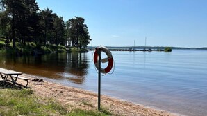 Ein Rettungsboje an einem sandigen Strand mit einem Picknicktisch und einem ruhigen See im Hintergrund.