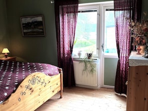 A bedroom with a wooden bed, a window with curtains, a radiator, and a bedside table with a lamp. - 4 Star Holiday Home in Karlsborg (Karlsborg)