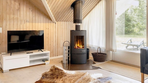 A modern living room with a large TV, a black wood-burning stove, and a view of the outdoors through a large window.