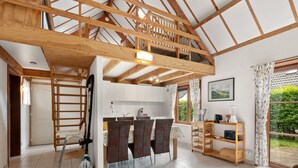 A spacious kitchen with a dining area, wooden beams, and a view of greenery outside. - Nice Holiday Home by the sea (De Haan)