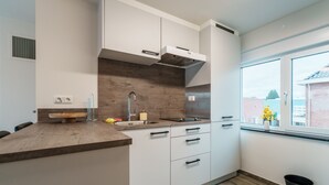 A modern kitchen with white cabinets, a wooden countertop, and a window with a view of the outside. - Cosy Apartment Near Center (Landgraaf)