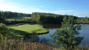 A golf course with a pond, surrounded by dense trees and clear skies. - Cosy Apartment Near Center (Landgraaf)