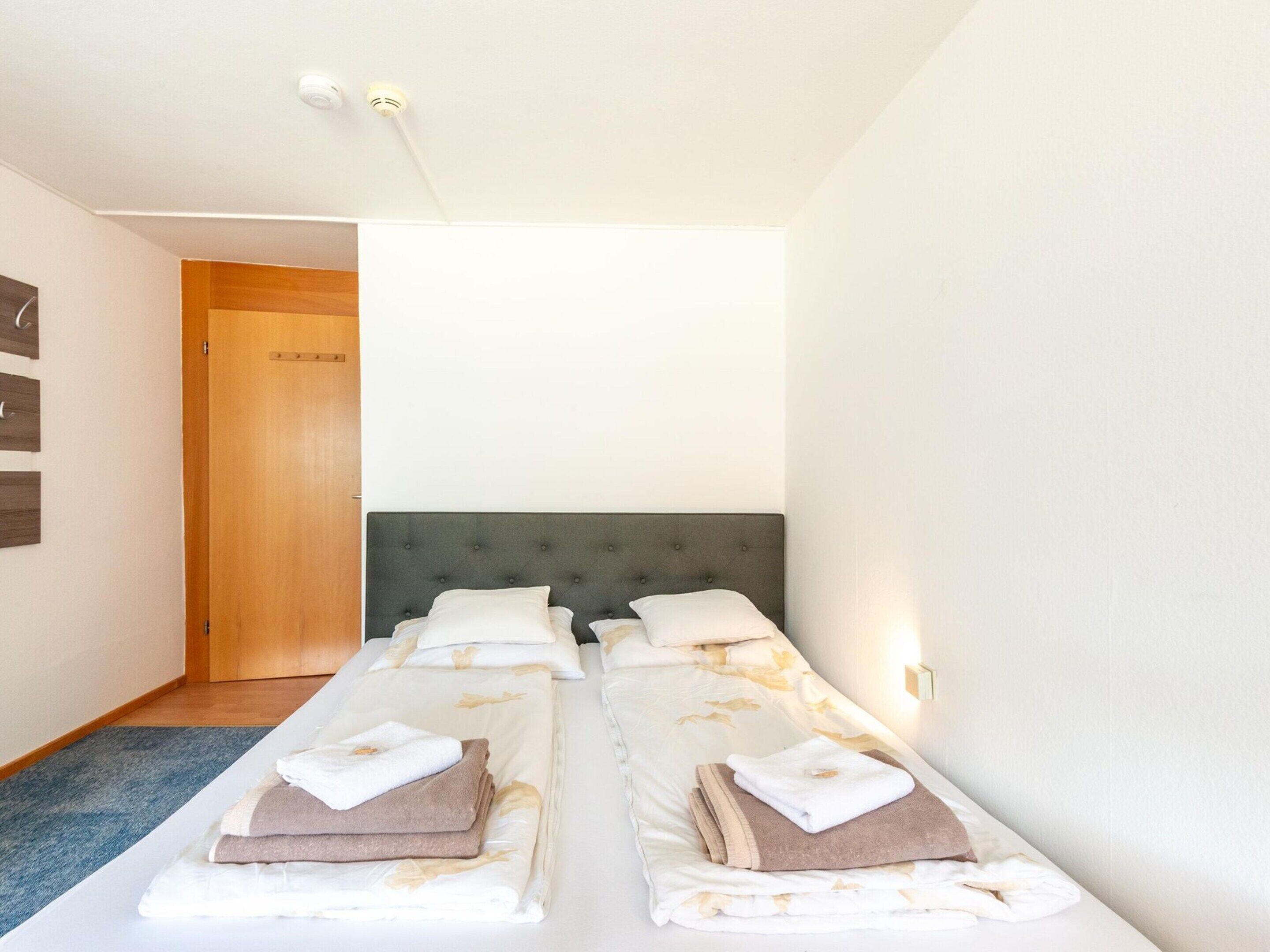 Una habitación de hotel con dos camas individuales, una puerta de madera, una alfombra azul y una pared blanca.