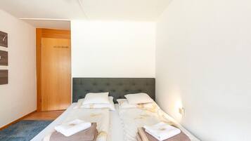 Una habitación de hotel con dos camas individuales, una puerta de madera, una alfombra azul y una pared blanca.