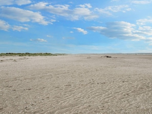 Una amplia playa arenosa con dunas y cielo despejado.