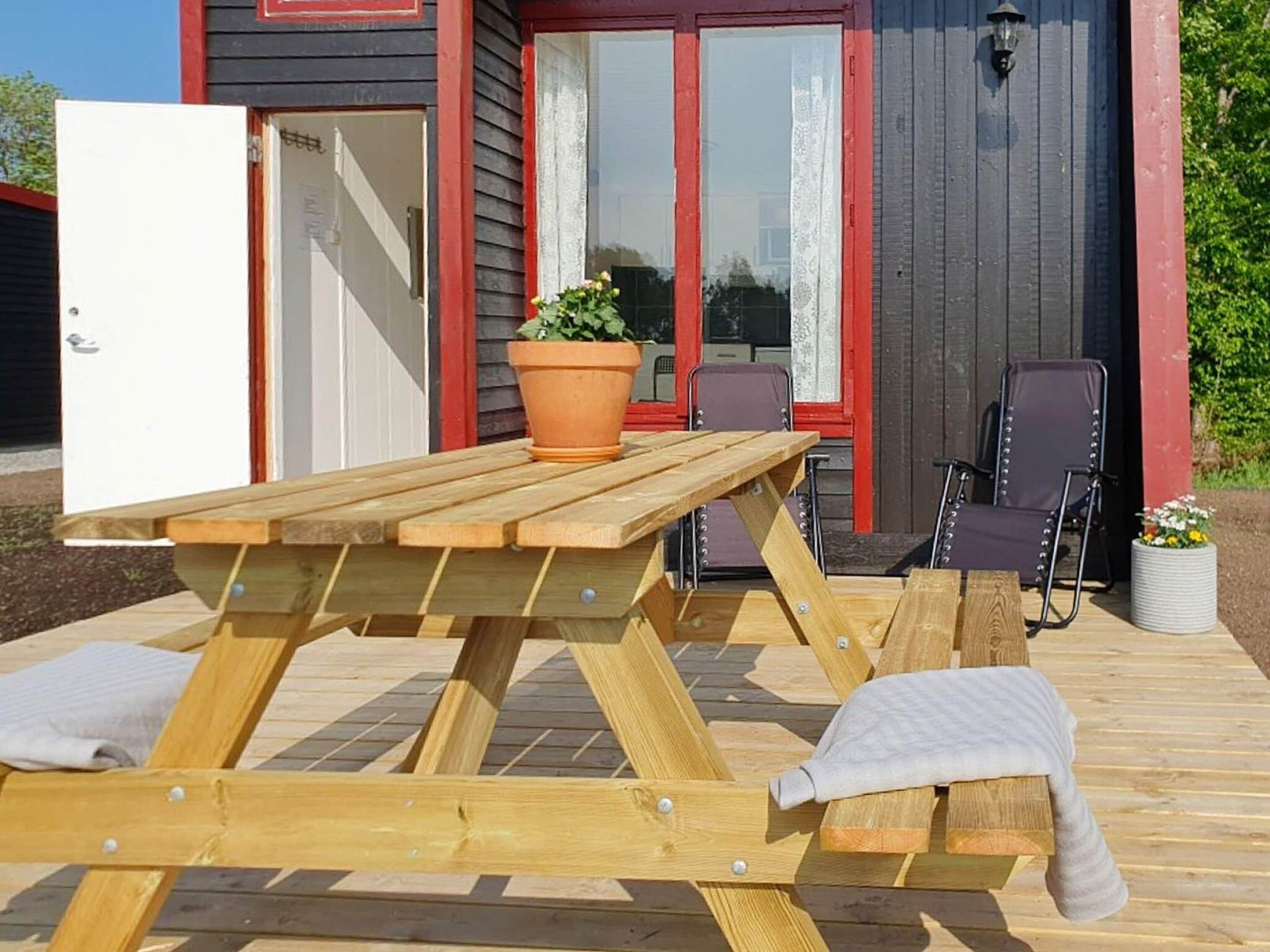 A wooden picnic table with cushions, a potted plant, and two chairs on a wooden deck.