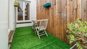 A small patio with artificial grass, a wooden table and chairs, a wooden fence, and a potted plant. - Ideal Holiday Home With Garage (Blankenberge)