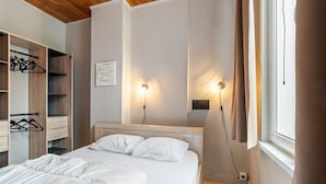 A bedroom with a bed, wooden headboard, bedside lamps, a wardrobe, and a wall with a light switch. - Ideal Holiday Home With Garage (Blankenberge)