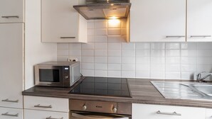 A modern kitchen with white cabinets, a built-in microwave, a stove, and a sink. - Ideal Holiday Home With Garage (Blankenberge)