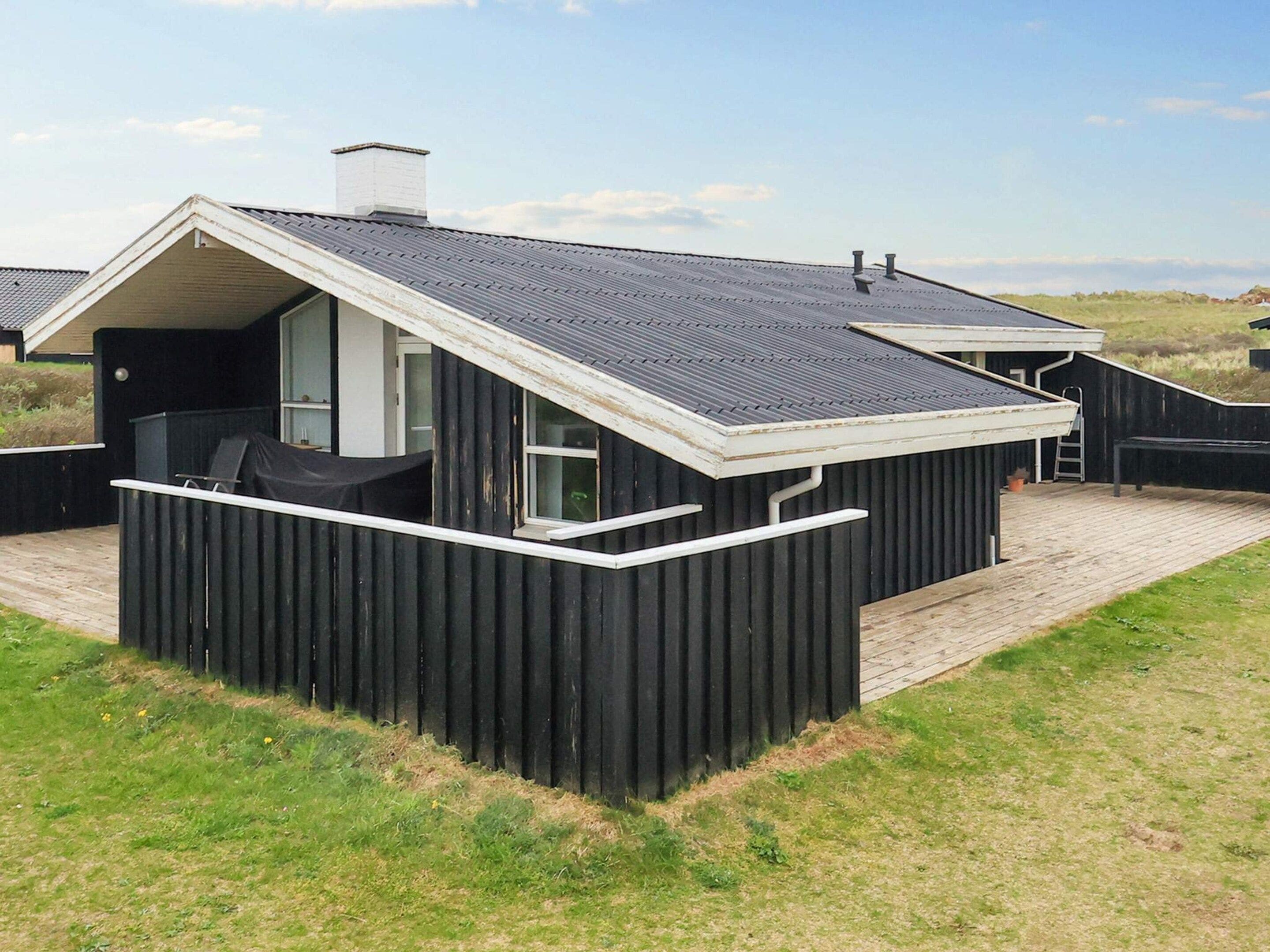 A small, black, single-story building with a sloped roof, a covered patio area, and a visible window.