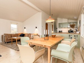 Ein modernes Wohnzimmer mit einem Holzespeisetisch, hellen Stühlen, einer Couch und einer Küchenzeile mit einem grünen Schrank und einer hängenden Lampenleuchte.