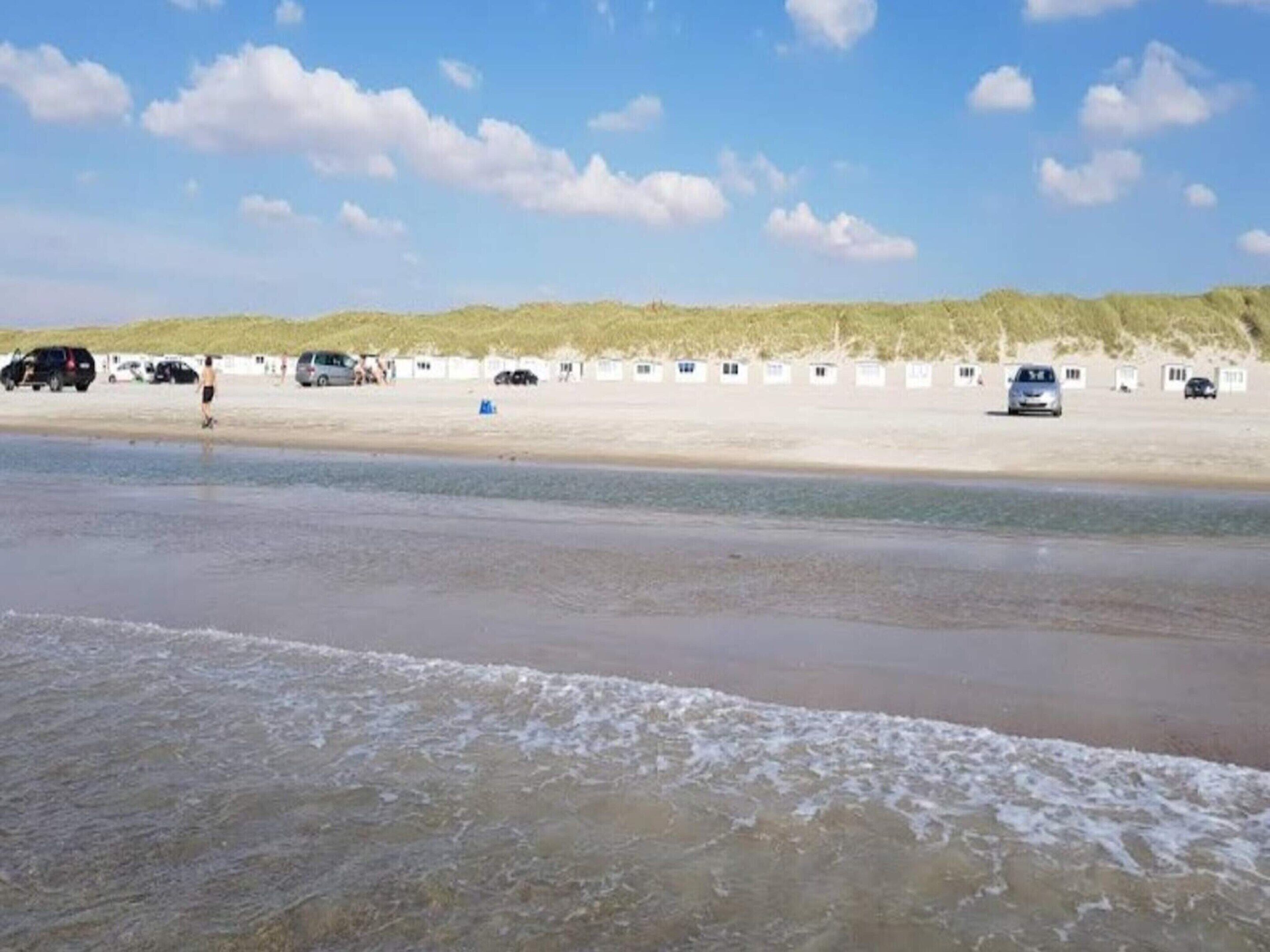 Une plage bordée d’une rangée de cabanes de plage blanches, un rivage sablonneux et un ciel dégagé.