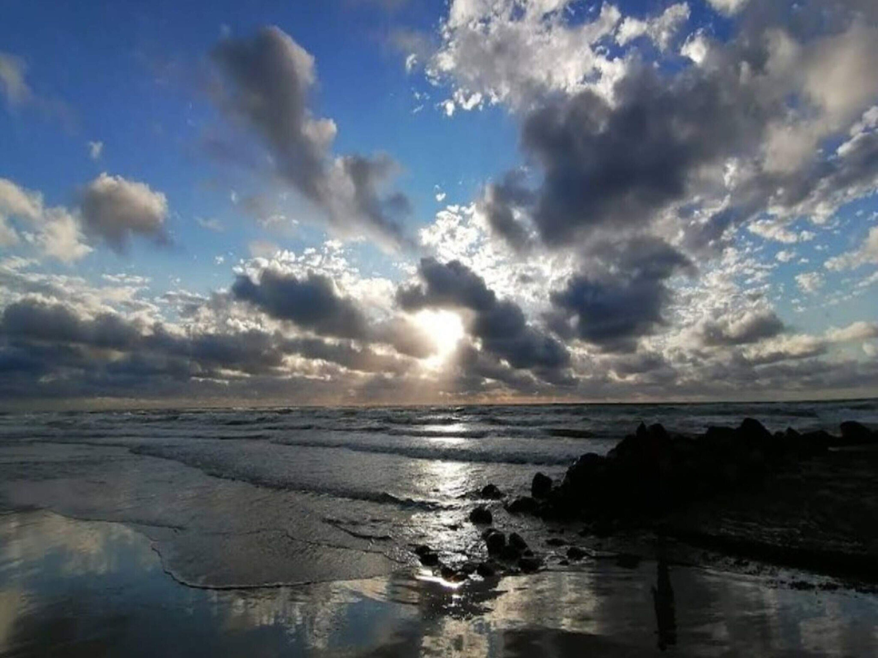 A beach with waves, rocks, and a cloudy sky.