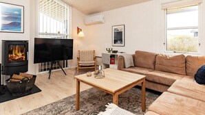 Ett vardagsrum med en öppen spis, en tv, en soffa, ett soffbord och en mönstrad matta.